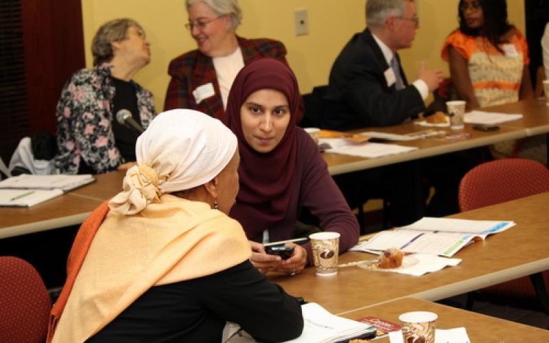 Two women converse at tables. Others chat behind them