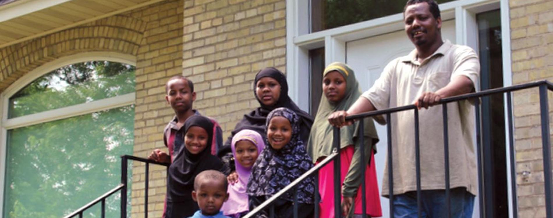 A family of seven on the steps outside a newly purchased brick home