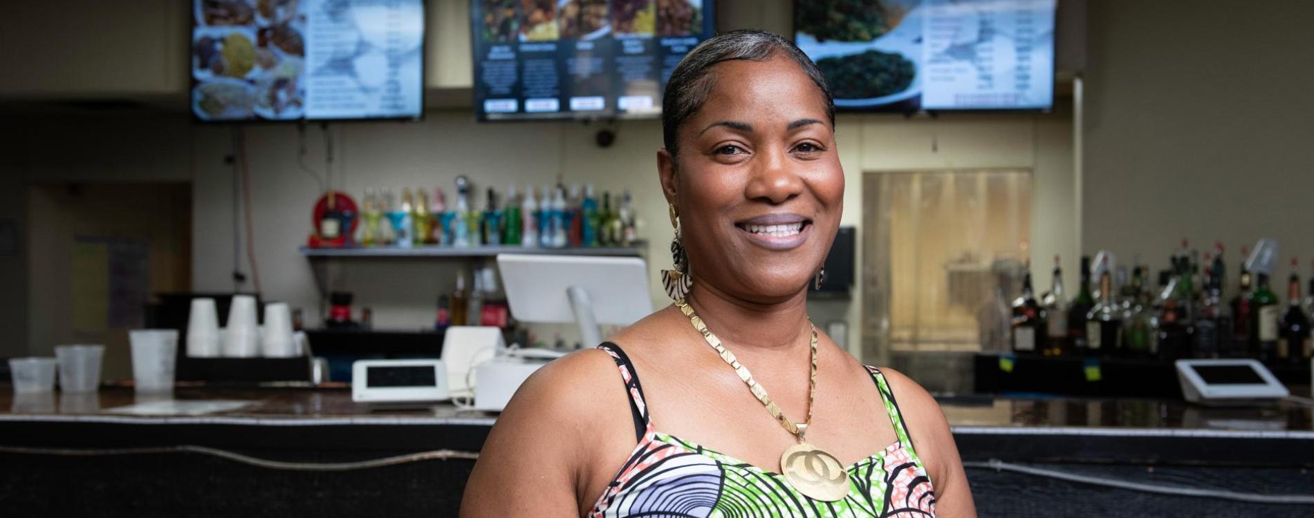 A woman of African descent welcomes viewers to her restaurant and night club.